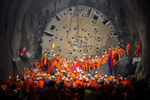 Miners hold national flags stand next to a giant drilling machine that completed the world