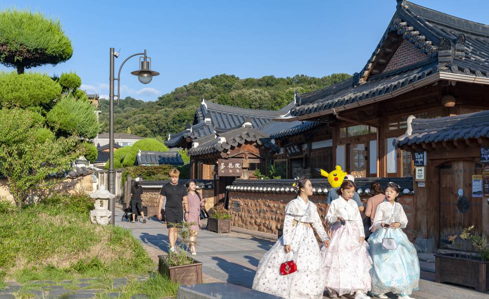 Turistas vestidas con el tradicional 'hanboknam' pasan ante uno de los 'hanoks' de aldea de Jeonju, en Corea del Sur. JIKGOE GETTY