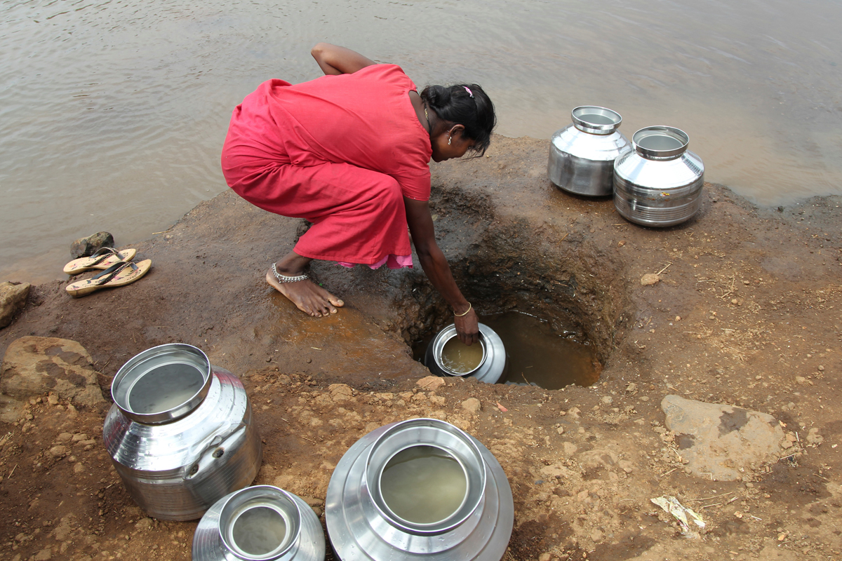 A woman fetches water from an opening made to filter water next to a polluted lake in Thane, India June 13, 2019. REUTERS/Prashant Waydande